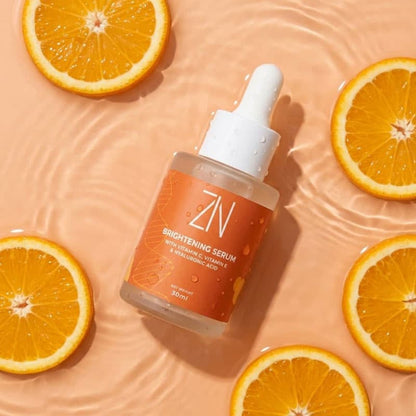 ZIN Brightening Serum bottle with dropper on a peach background with orange slices